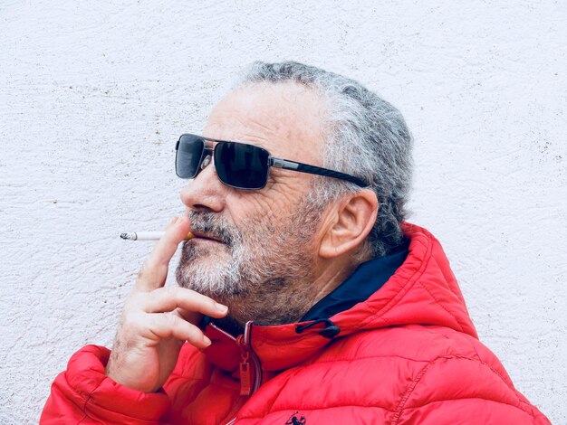 Foto close-up di un uomo anziano che fuma una sigaretta contro il muro