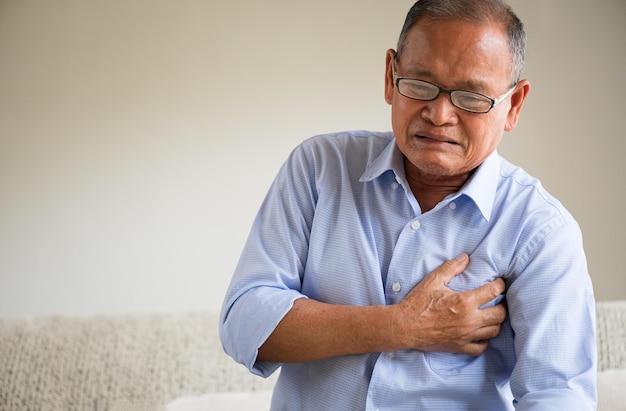 Close Up senior mannelijke Aziatische lijden aan hevige pijn in zijn hartaanval op de borst thuis. Gezondheidszorg en medisch concept van senior hartziekte.