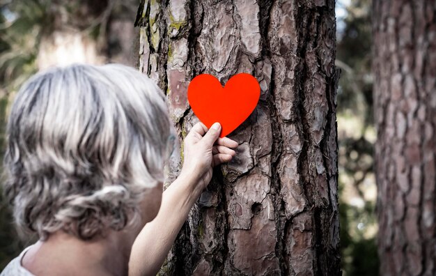 Foto close-up di una donna anziana che tiene una forma di cuore sul tronco di un albero