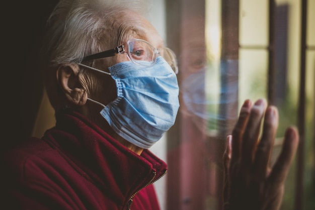 Photo close-up of senior woman wearing mask with reflection on window