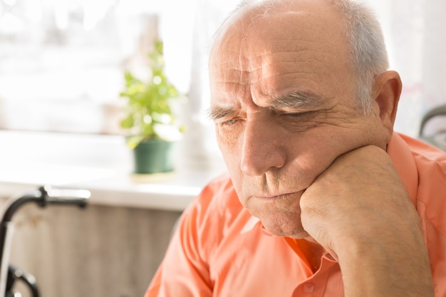 Close-up serieuze senior kale man, in oranje shirt, neerkijkend met vuist op zijn gezicht