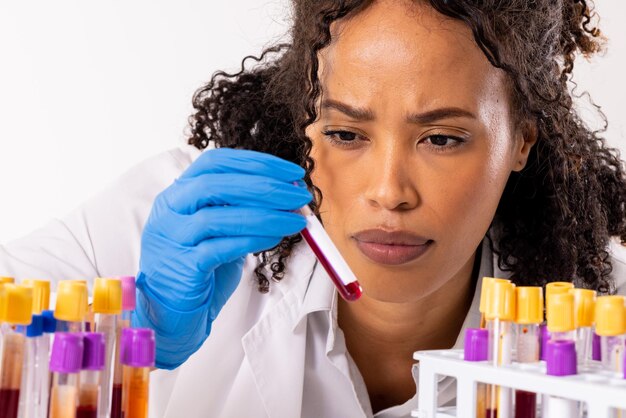 Foto primo piano del medico femminile africano americano serio della metà di adulto che indossa la provetta della tenuta del guanto. concetto di sangue, provetta, medicina, campione, laboratorio, medico, assistenza sanitaria e occupazione medica.