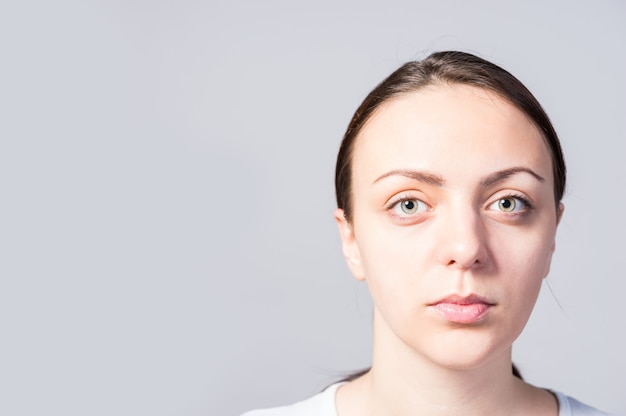 Close up Serious Face of a Young Woman Looking at the Camera Against Light Gray Wall with Copy Space.