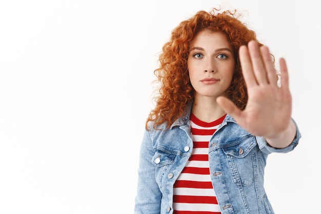 Close-up serious-looking persuasive redhead attractive female model demand stop hold on extend palm camera taboo enough gesture give restriction ban bad choice, standing white wall