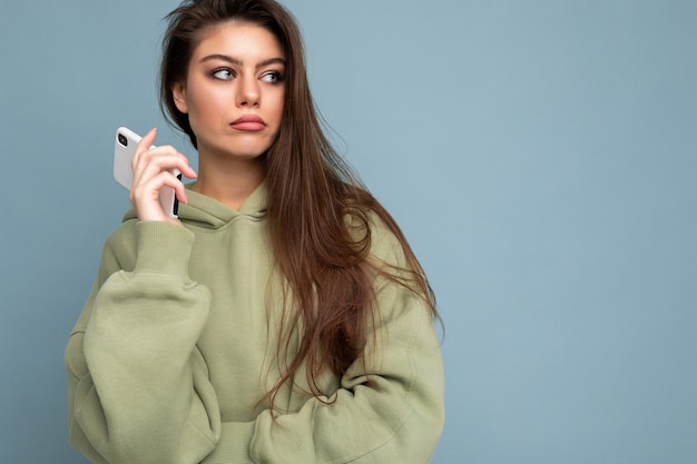 Close up of serious upset attractive young woman wearing stylish hoodie holding using mobile phone