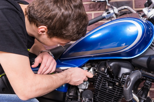 Photo close up serious young guy fixing his blue sports motorbike using a wrench tool.