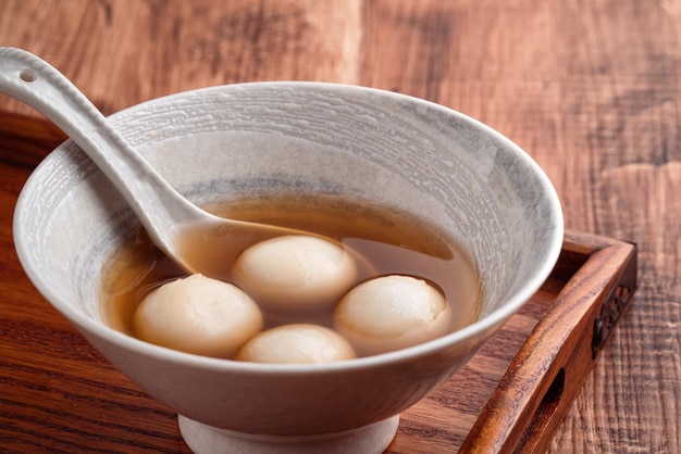 Primo piano di sesamo grande tangyuan (tang yuan, palline di gnocco di riso glutinoso) con zuppa di sciroppo dolce in una ciotola sul fondo della tavola di legno per il cibo del festival del solstizio d'inverno.