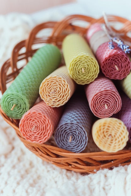 Close up of set of colored decorative natural beewax candles with a honey aroma for interior in a basket on a white knitted sweater