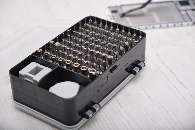 A close-up of a set of screwdriver bits in a black box, gloves, a broken smartphone and a set of tools for replacing the glass of the phone and tablet