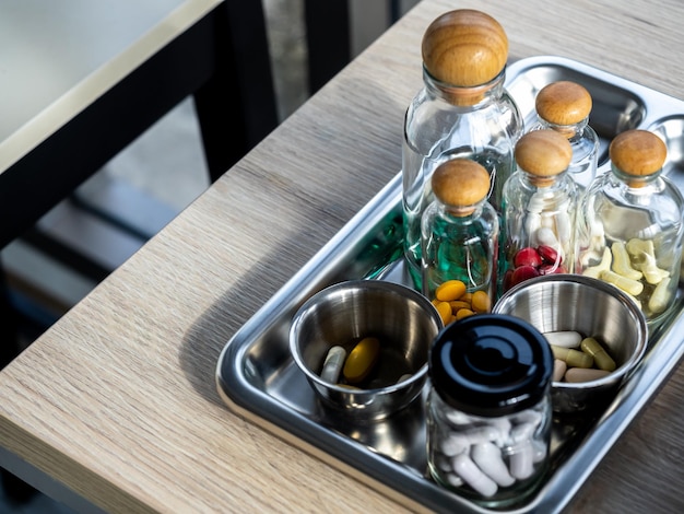 木製のテーブルの鋼の医療トレイにある小さな透明なガラス瓶のビタミンとサプリメントのセットをクローズアップ緑黄赤白のビタミングループヘルスケアと医療の概念