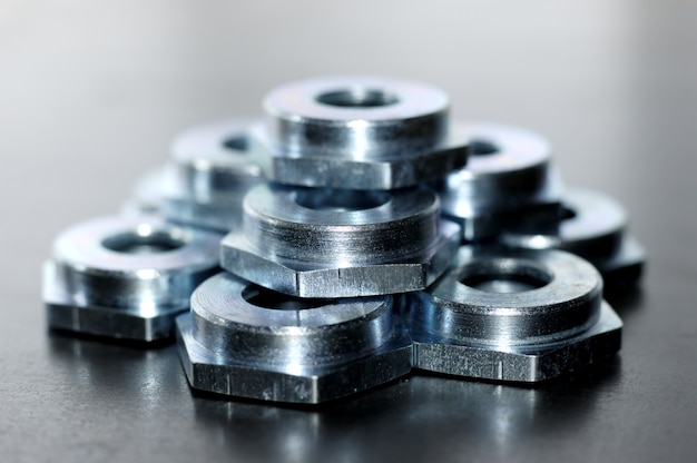 Close up of several flat metal nuts lying on a metal surface in a workshop