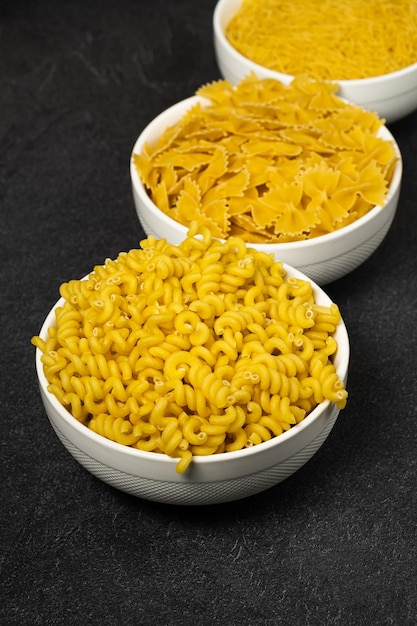 Close up of several types of dry pasta in a plate on dark background