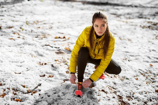 Закройте вверх девушки фитнеса формы в sportswear связывая шнурки в солнечном утре зимы снаружи в природе.