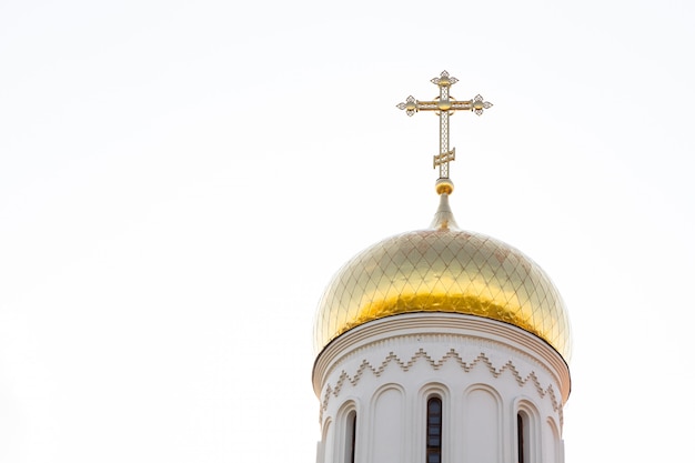 Close-up of shiny sunlit christian church dome with cross on top against white sky