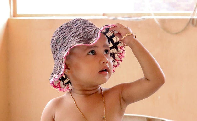 Photo close-up of shirtless baby girl wearing bucket hat at home