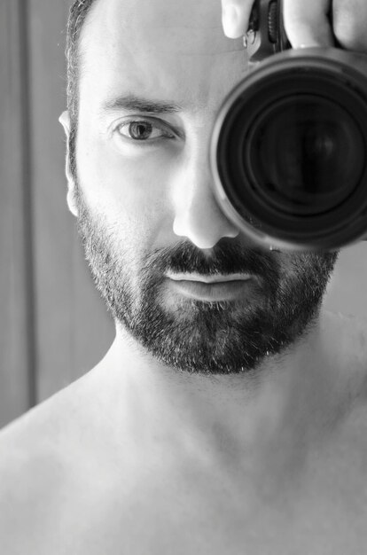 Close-up of shirtless man looking through dslr camera