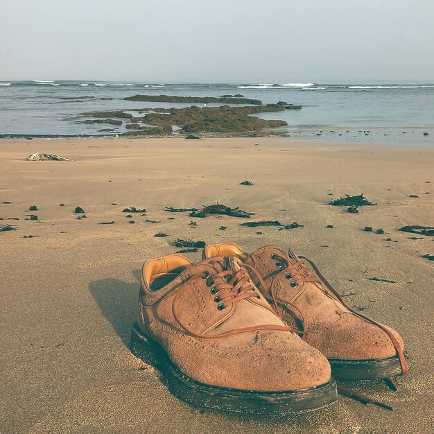 Photo close-up of shoes on beach against sky