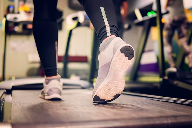 Close up shoes woman's muscular legs feet running on treadmill workout at fitness gym Show of running shoes rubber floor softness