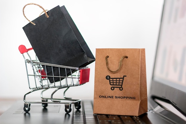 Close-up of shopping bags with cart and laptop against white background