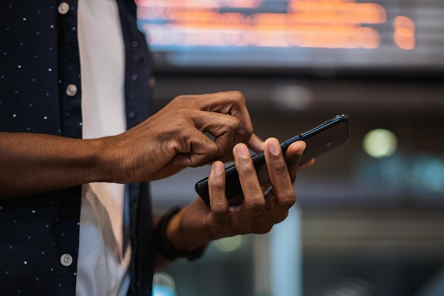 Immagine ravvicinata di un uomo africano che invia un messaggio di testo al telefono è in una stazione ferroviaria