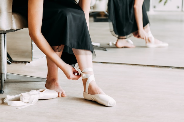 Close-up shot of a ballerina taking off the ballet shoes sitting on the floor 