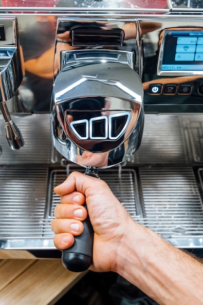 Close-up shot of barista holding filter holder while coffee machine brewing fresh espresso into glass