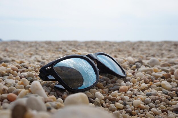 Close up shot of black sunglasses on pebble beach with reflective blue sky