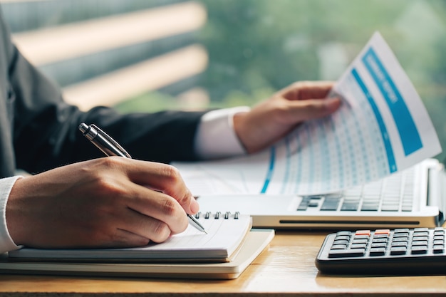 Close up shot of business man hands with pen writing notes on a paper and other hand holding the marketing chart. 