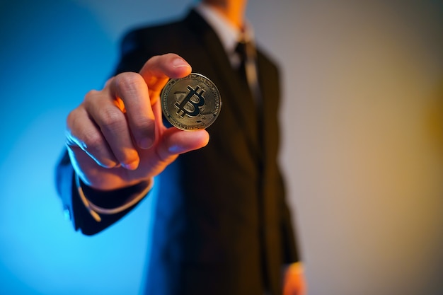 Photo close up shot of businessman in black suit holding golden coin isolated on background.