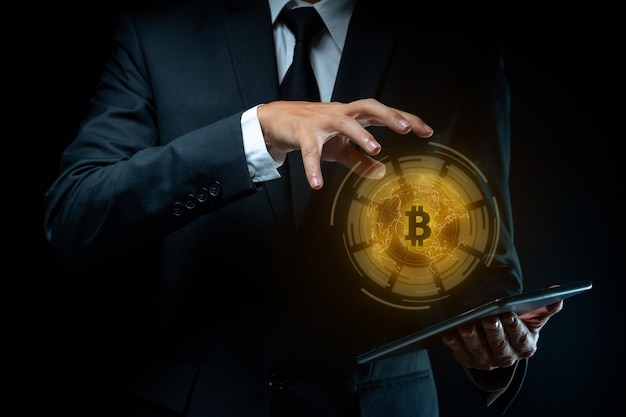 Close up shot of Businessman in black suit holding tablet with bitcoin symbol hologram effect.