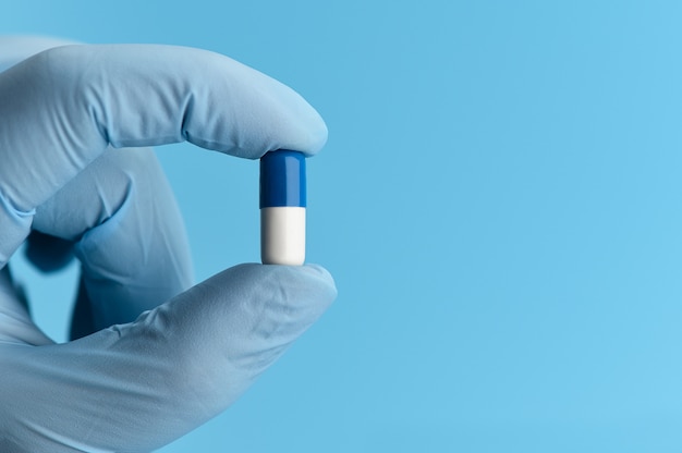 Close-up shot of capsule pill in nurse's hand on blue background. female hand in a medical glove is holding an antiviral capsule.