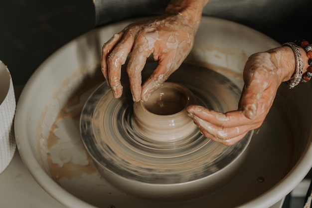 Photo close-up shot of ceramic cup spinning on potterss wheel and hands molding clay