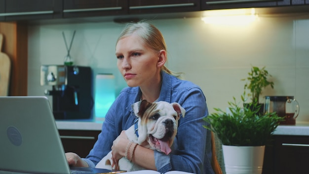 Close-up shot of cheerful woman hugging small dog in the kitchen