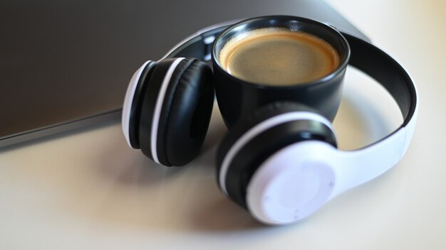 Close-up shot of Coffee mug with laptop and headphone on placed on a table in a cafe,Coffee mug place in headphone.