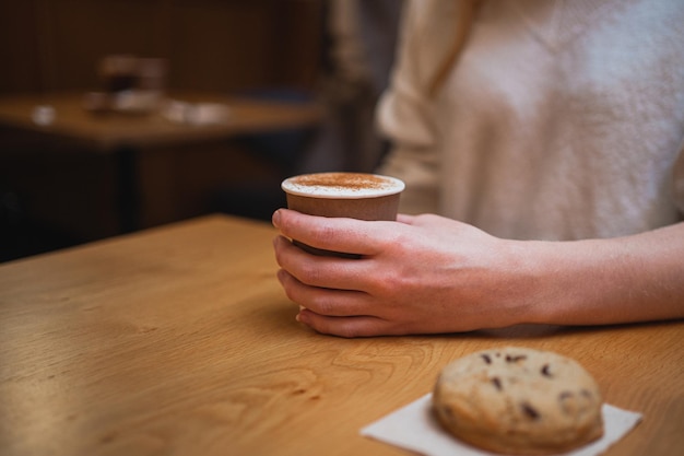 コーヒー ショップ内の若い女性とチョコレート クッキーが保持しているコーヒー カップのショットを閉じる