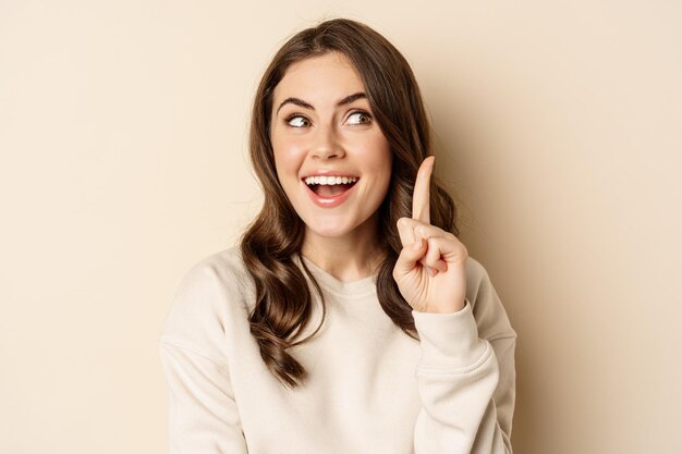 Close up shot of excited woman looking amazed with opened mouth standing over beige background person