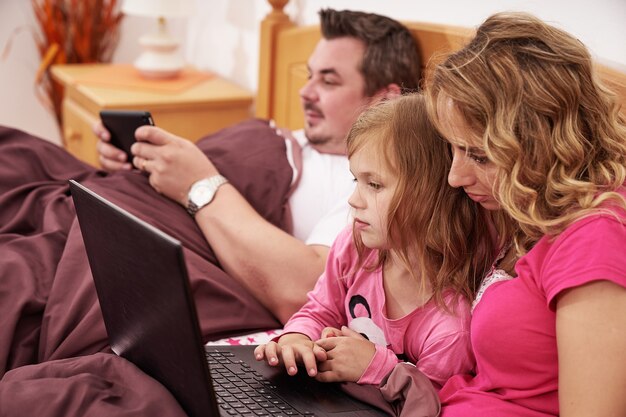 Снимок семьи, использующей цифровые устройства, лежа в постели по утрам крупным планом