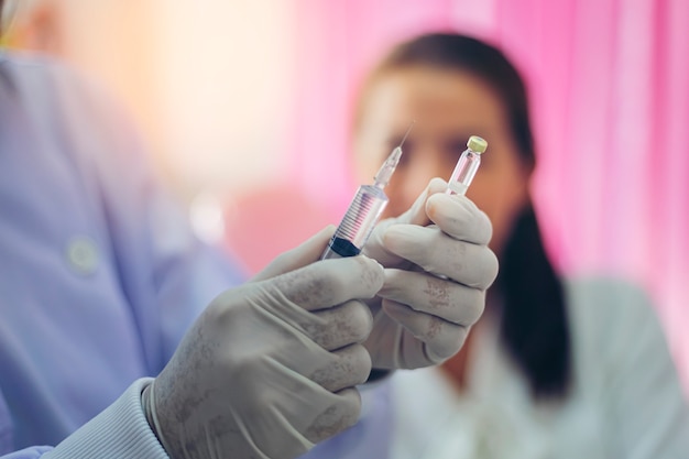 Close-up shot of a female doctor holding a syringe to prepare for the injection of the patient sitting with a thrilling look