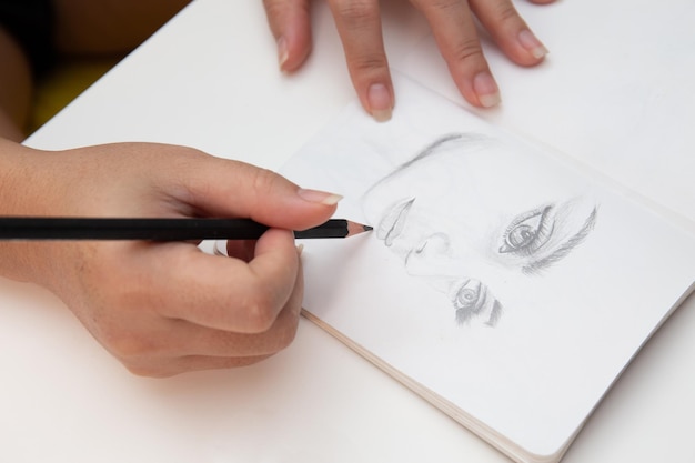 Photo close up shot of female hand drawing and sketching her face on notebook