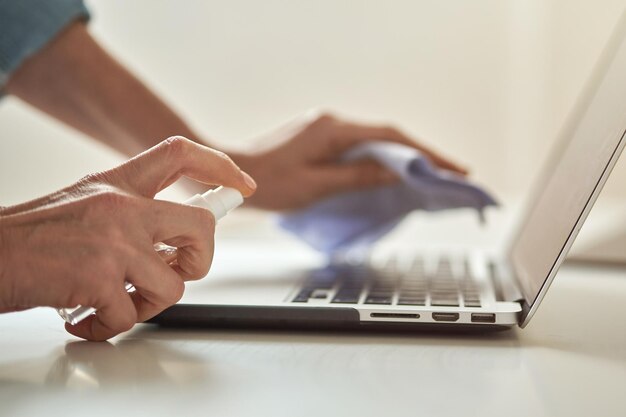 Close up shot of female hands using antibacterial sanitizer spray while disinfecting laptop