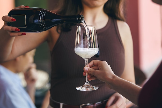 Close up shot of female sommelier pouring sparkling wine to guest on outdoor
