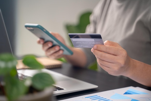 Close up shot of females hands holding credit card typing message on smart phone for shopping online at home office