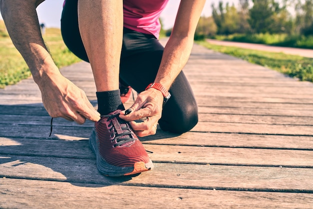 Close up shot of fit man tying shoelaces on wooden path. Sunny bright day.