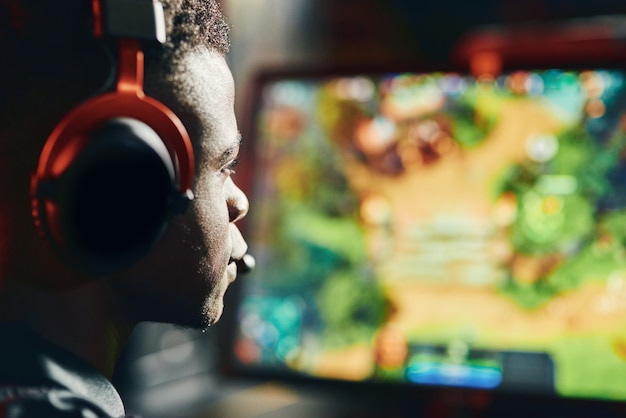 Close up shot of a focused african guy professional cybersport gamer wearing headphones playing