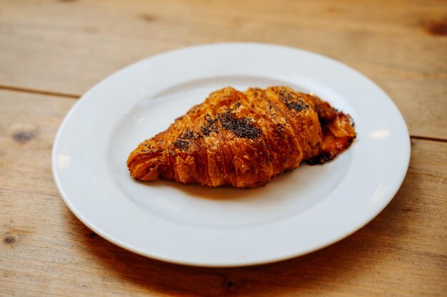 Close up shot of a fresh croissant with poppy seeds laying on a white plate