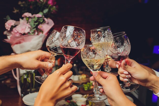 Close up shot of group of people clinking glasses with wine or champagne in front of bokeh background. older people hands.