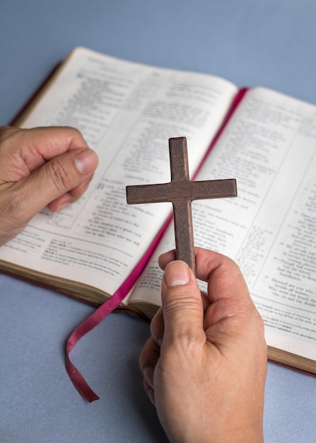 Close up shot of hand holding a religious cross crucifix on top\
of holy bible