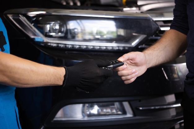 Close up shot of hands of mechanic giving car key to male client after servicing in auto repair shop