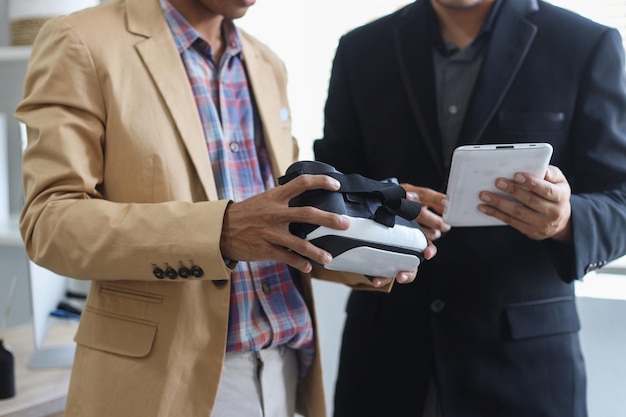 Close up shot of hands of two men in suit holding VR glasses headset and tablet