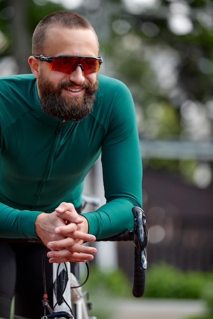 Immagine ravvicinata di un giovane europeo attraente felice con la barba che indossa occhiali e abbigliamento sportivo verde che guarda l'obbiettivo durante la corsa serale nel parco nel fine settimana